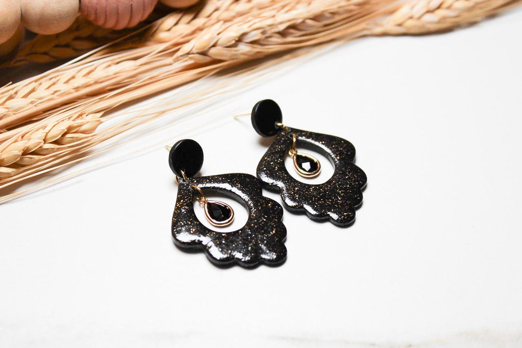Black floral earrings on a white surface with straw mat in the background