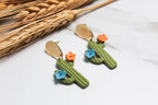 Cactus-shaped earrings with colorful flowers on a white surface with wheat stalks.