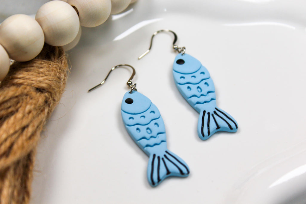 Blue fish-shaped earrings on a white surface with beads and twine.