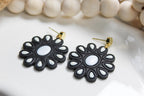 Black and white flower-shaped earrings on a white dish with beige beads in the background