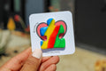 Colorful puzzle-shaped pin with a rainbow design held by a hand against a blurred background