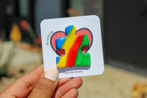 Colorful puzzle-shaped pin with a rainbow design held by a hand against a blurred background