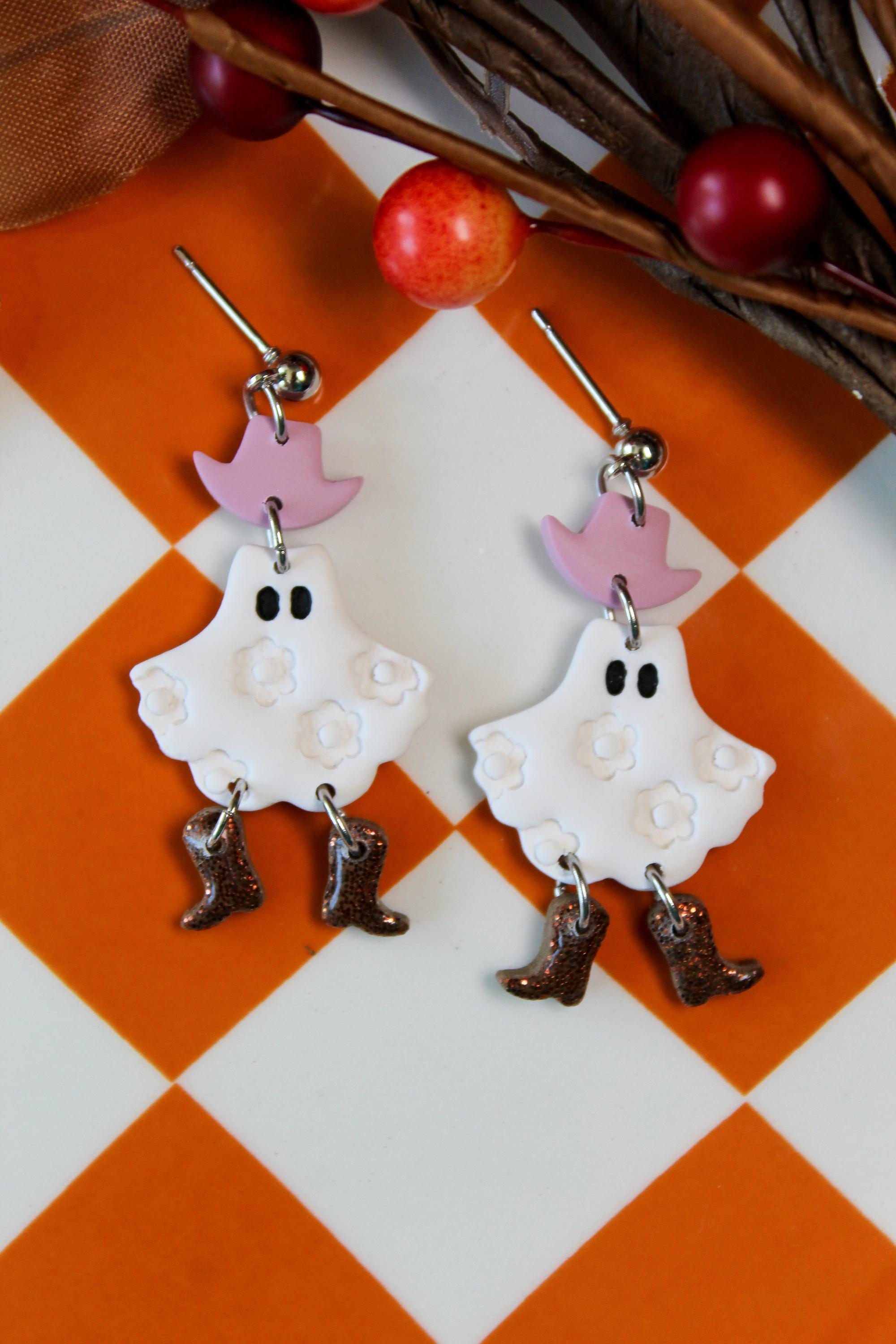 Ghost-shaped earrings with purple hats and brown boots on a checkered background