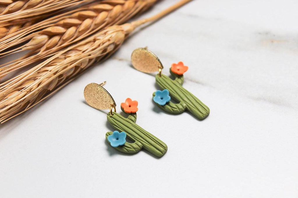 Cactus-shaped earrings with colorful flowers on a light background