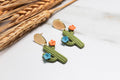 Cactus-shaped earrings with colorful flowers on a light background