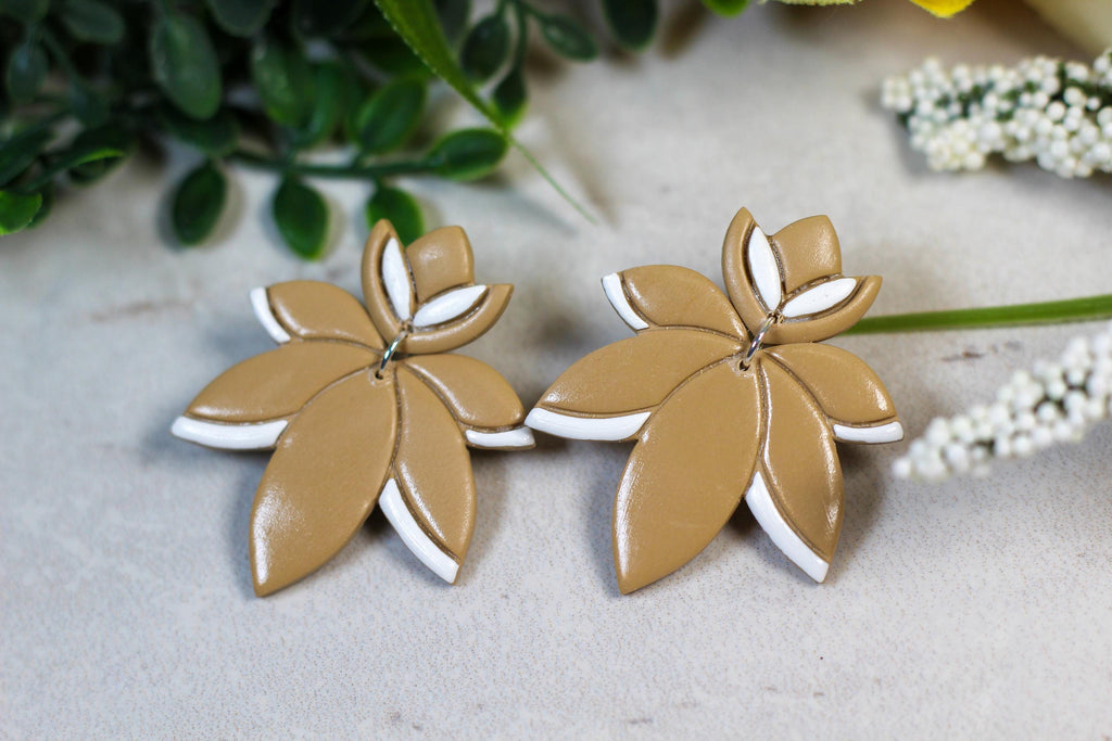 Pair of leaf-shaped earrings on a light surface with greenery in the background