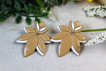 Pair of leaf-shaped earrings on a light surface with greenery in the background