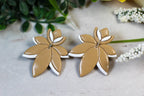 Pair of leaf-shaped earrings on a light surface with greenery in the background