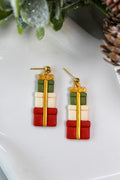 Christmas-themed gift box earrings on a white plate with greenery and pine cones.