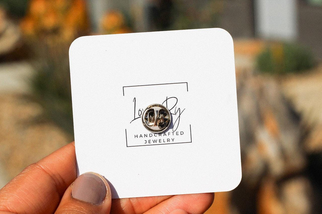 Handcrafted pin card held by a hand with blurred outdoor background
