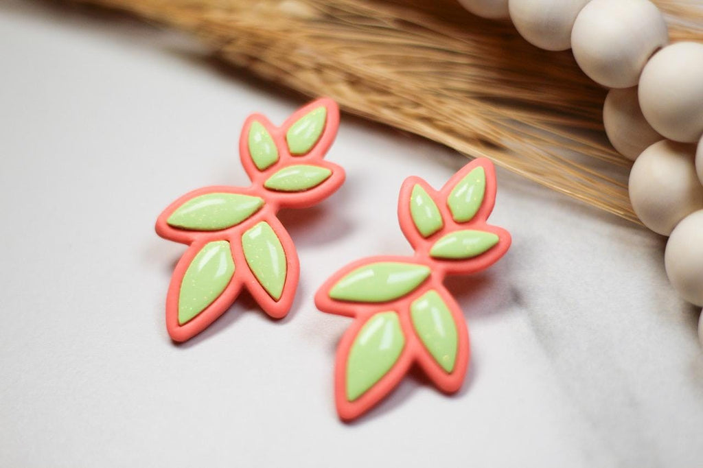Pair of pink and green leaf-shaped earrings on a light background