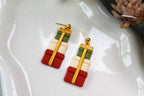 Christmas-themed gift box earrings on a white plate with greenery and pine cones.