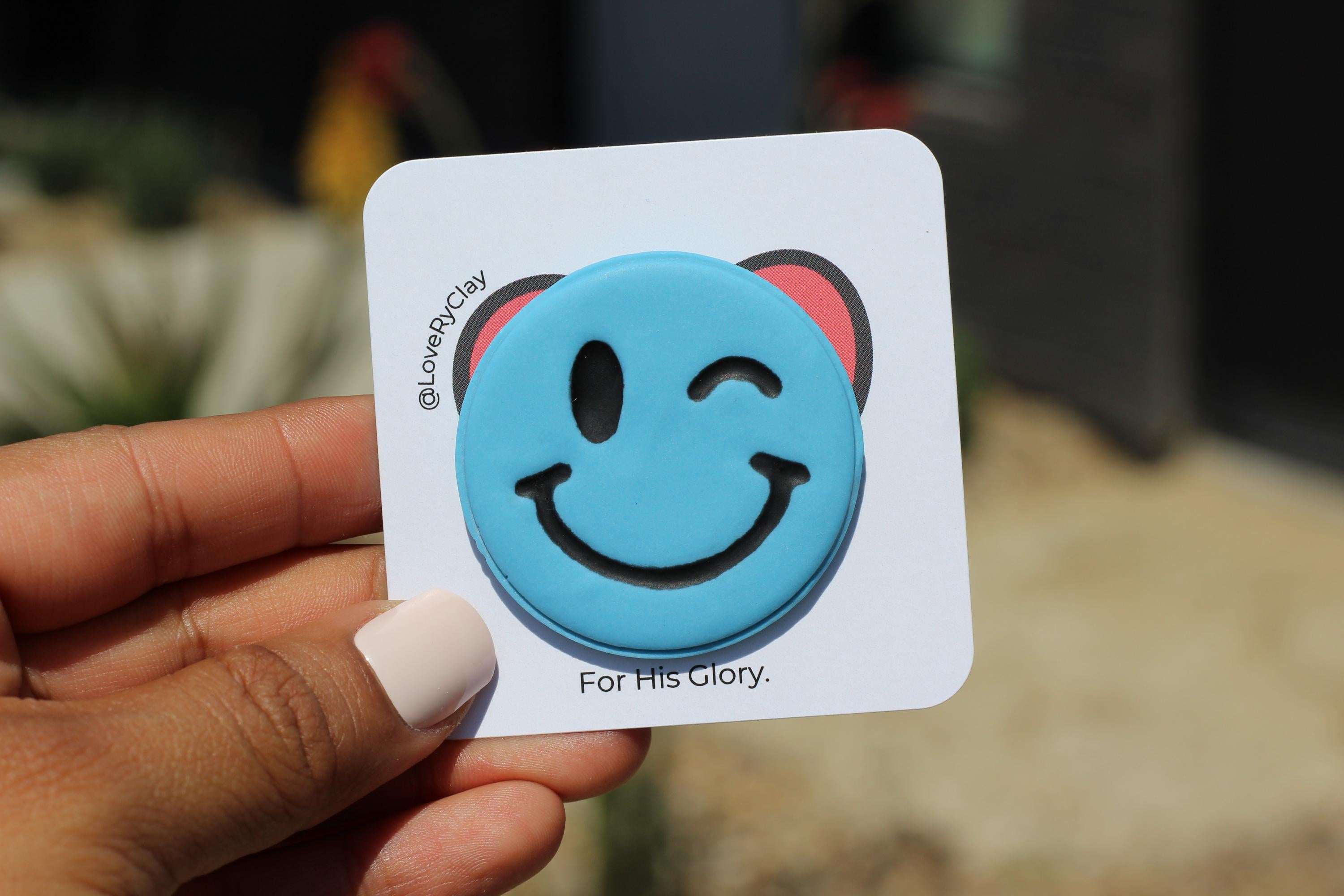 Hand holding a blue smiley face pin with on a white card