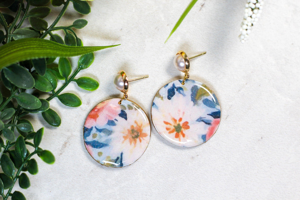 Floral earrings on a white surface with green leaves in the background
