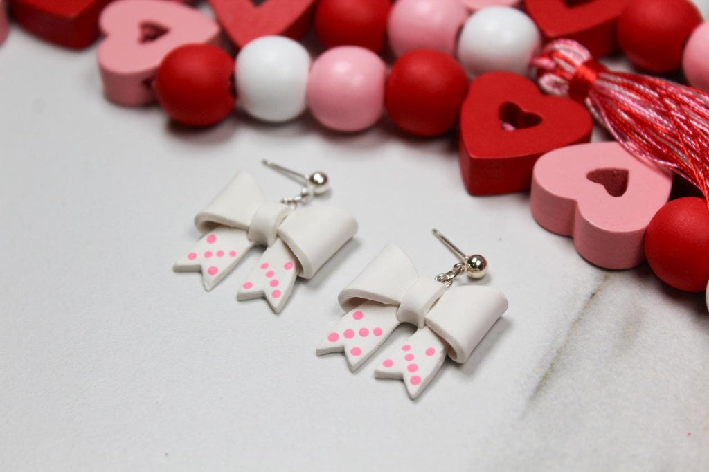 White bow-shaped earrings with pink centers on a white background with heart-shaped objects.
