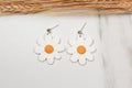 White flower-shaped earrings with yellow centers on a light background