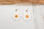 White flower-shaped earrings with yellow centers on a light background