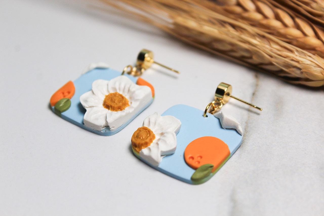 Pair of floral and peaches earrings on a light background with dried grass.