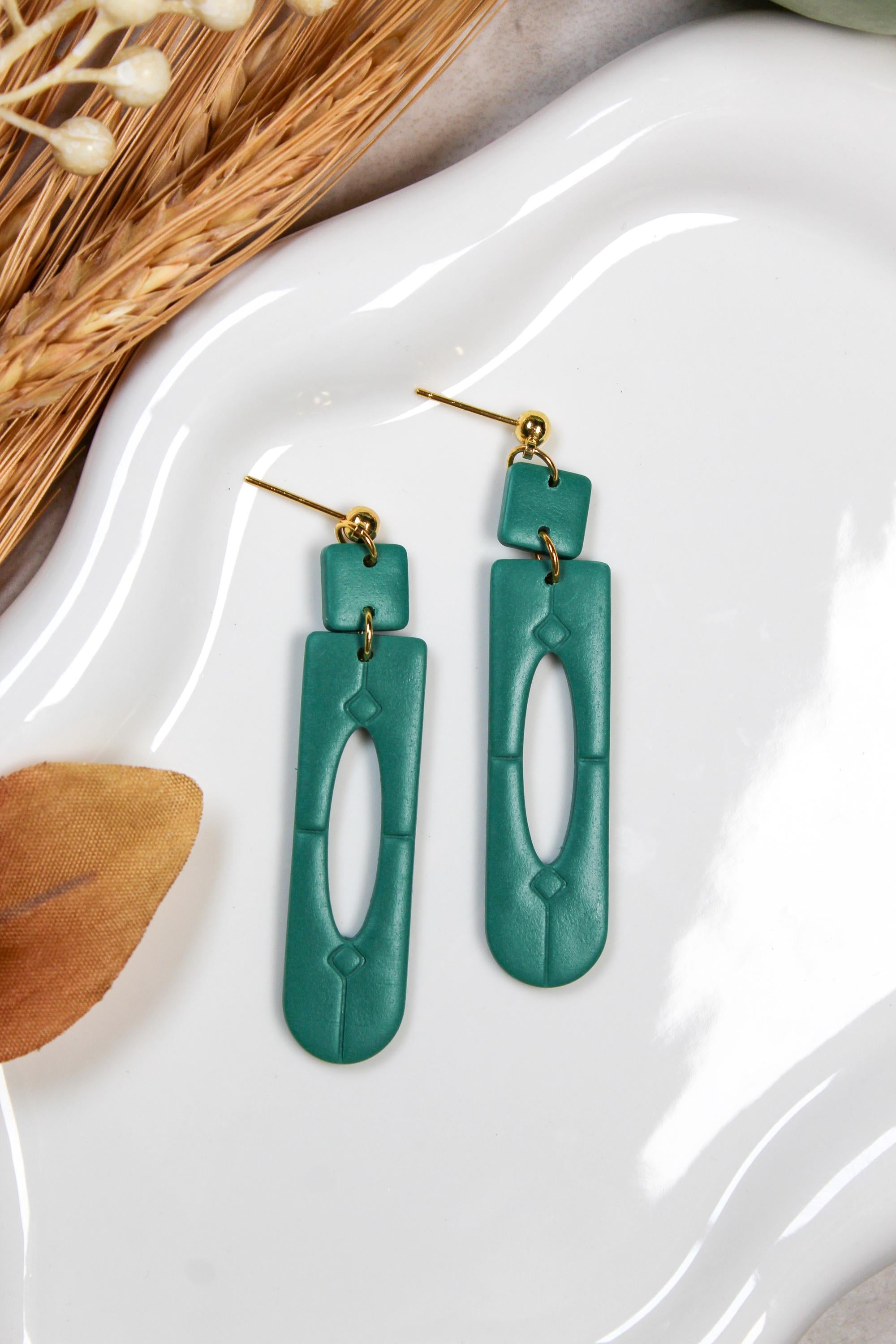 Teal earrings on a white dish with dried plants