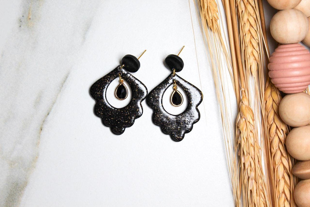 Black earrings on a white marble surface with wooden bead decor in the background