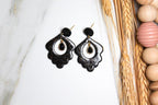 Black earrings on a white marble surface with wooden bead decor in the background