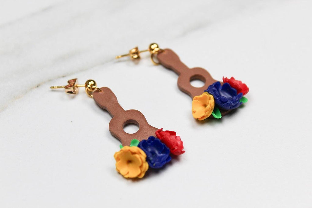 Pair of earrings shaped like guitars with floral tops on a light background