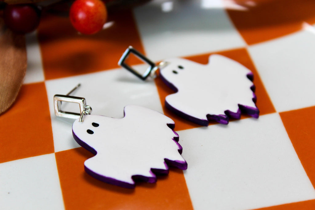 White ghost-shaped earrings with purple accents on a checkered surface
